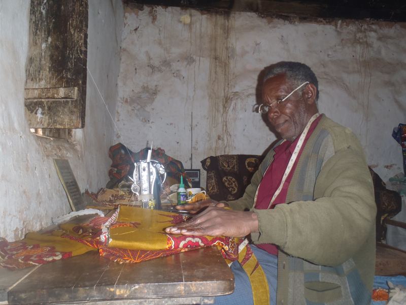 A tailor in Bumbuli works at his sewing machine with a length of printed kitenge cloth